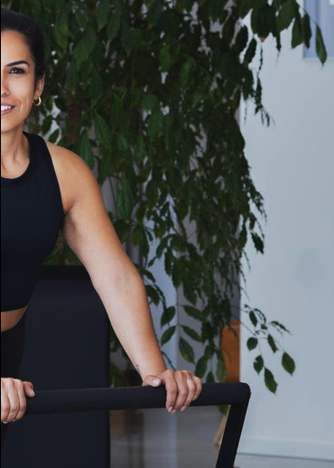 Lächelnde Frau in schwarzer Sportkleidung am Reformer im Studio von Reform by Physiotherapie in Köln-Mülheim